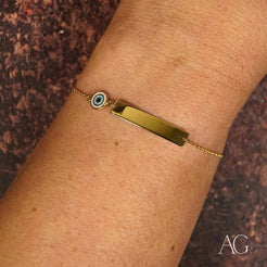 Delicate gold kids ID bracelet featuring evil eye motif and rectangular bar charm