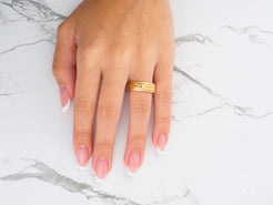 Gold wedding band from Stellar Strands on a finger with pink manicured nails