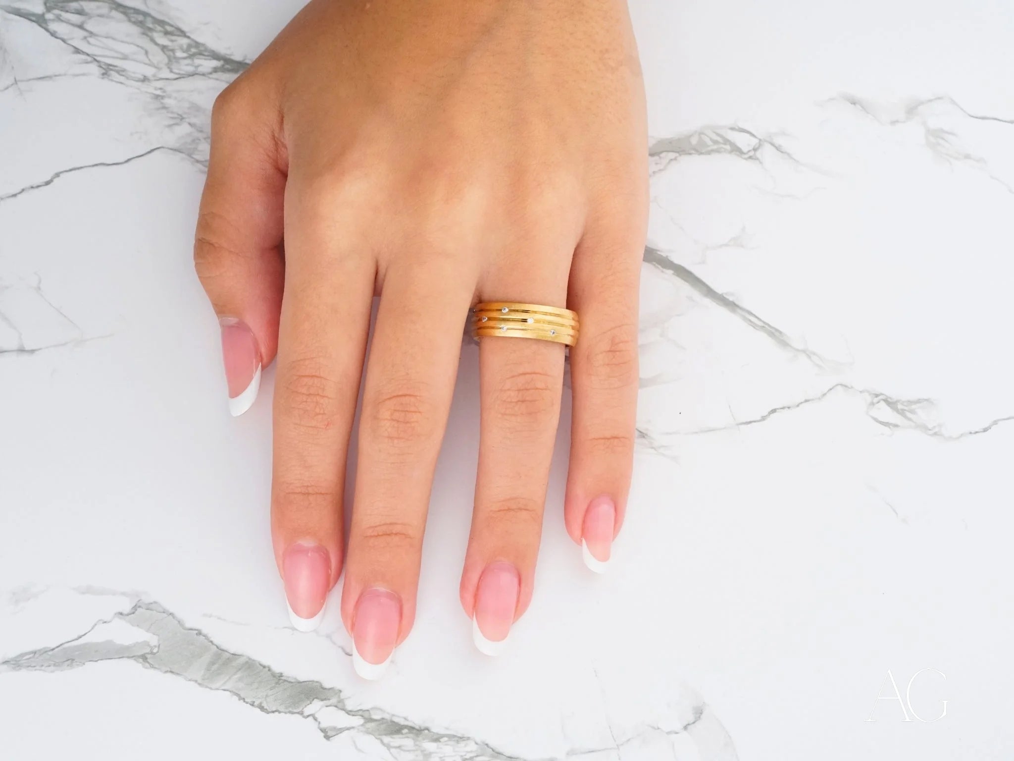 Gold wedding band from Stellar Strands on a finger with pink manicured nails