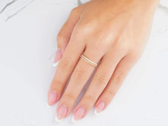 Delicate silver ring on a woman’s finger with pink nails, showcasing 18k yellow gold elegance