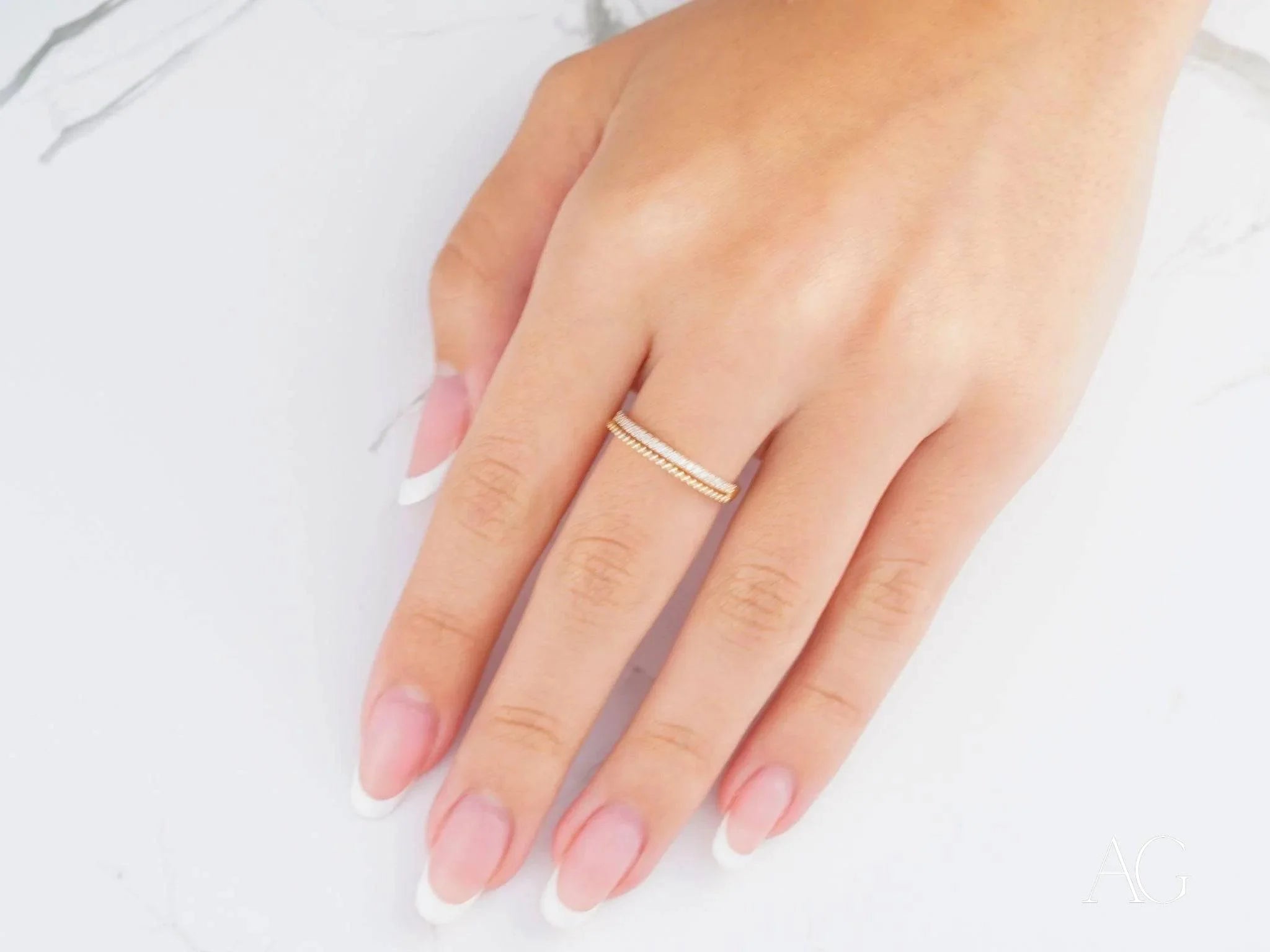 Delicate silver ring on a woman’s finger with pink nails, showcasing 18k yellow gold elegance