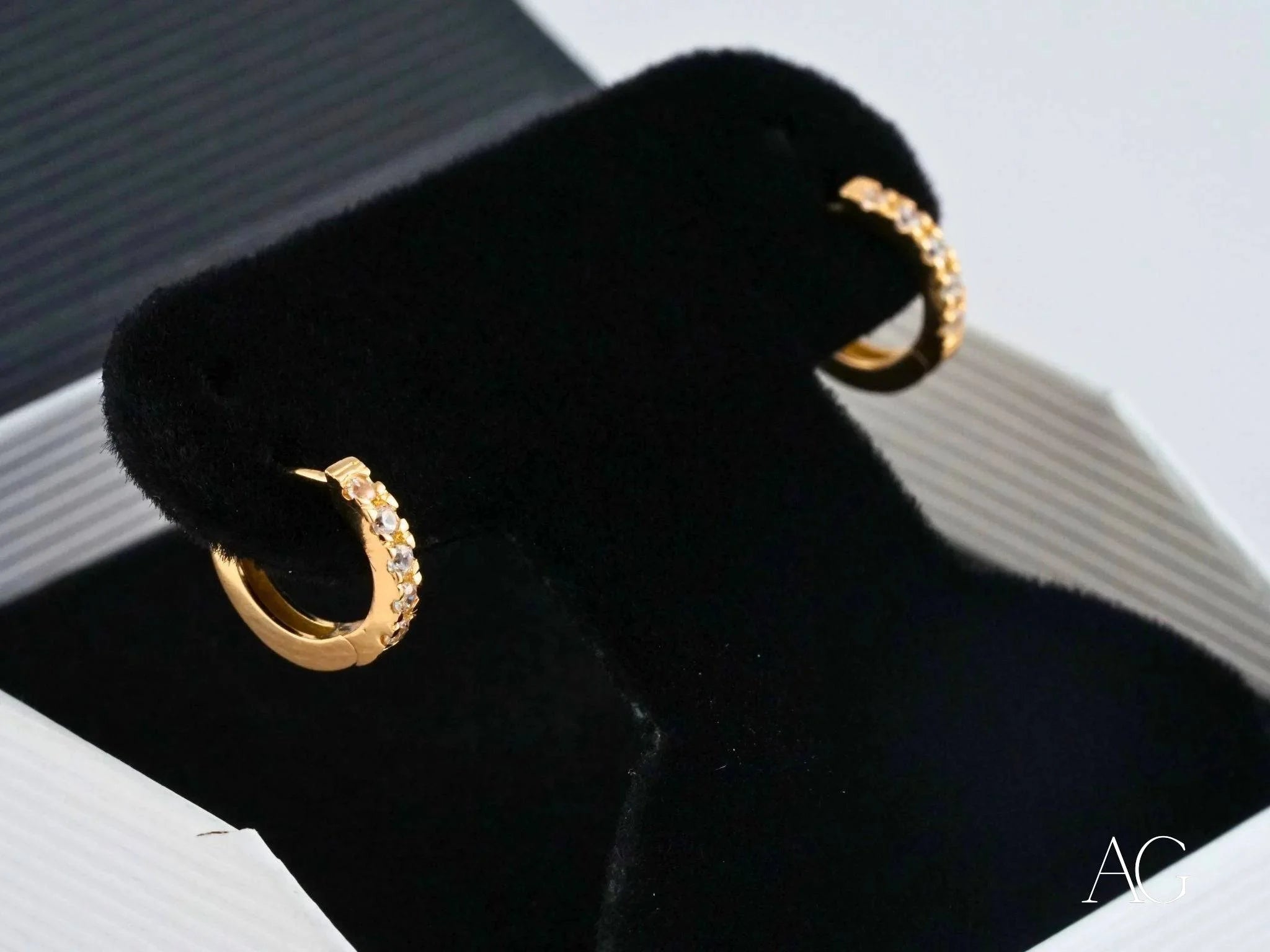 Gold hoop earrings with textured surfaces on a black stand, showcasing 18k yellow gold elegance